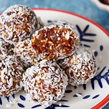 A stack of coconut date balls on a plate with the top ball cut open.