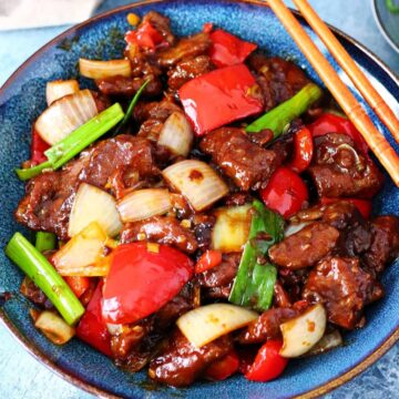 Beijing Beef with peppers and onions in a blue plate and chopsticks on the side.