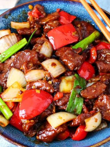 Beijing Beef with peppers and onions in a blue plate and chopsticks on the side.