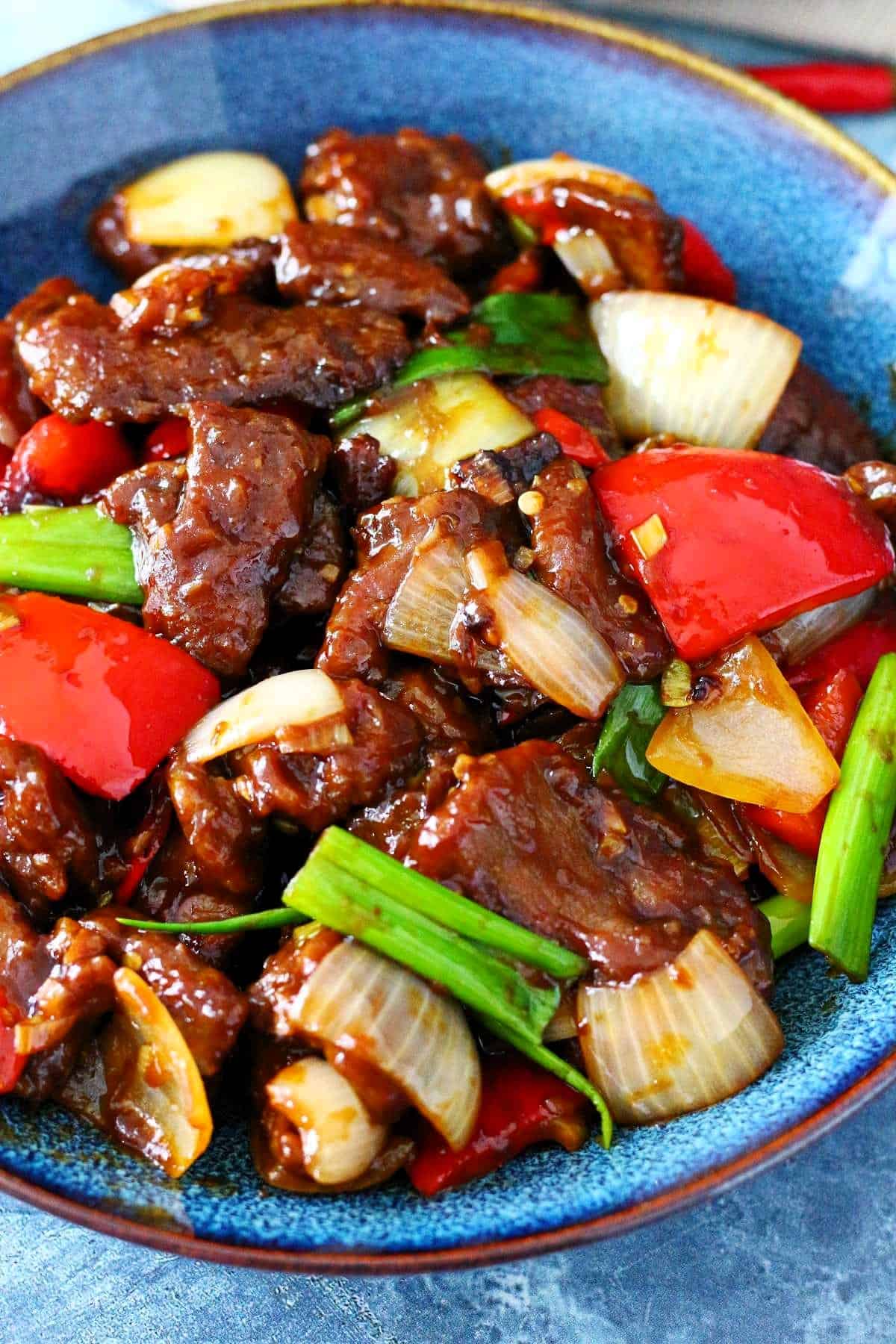 Beijing Beef with cubed peppers and onions in a blue plate.