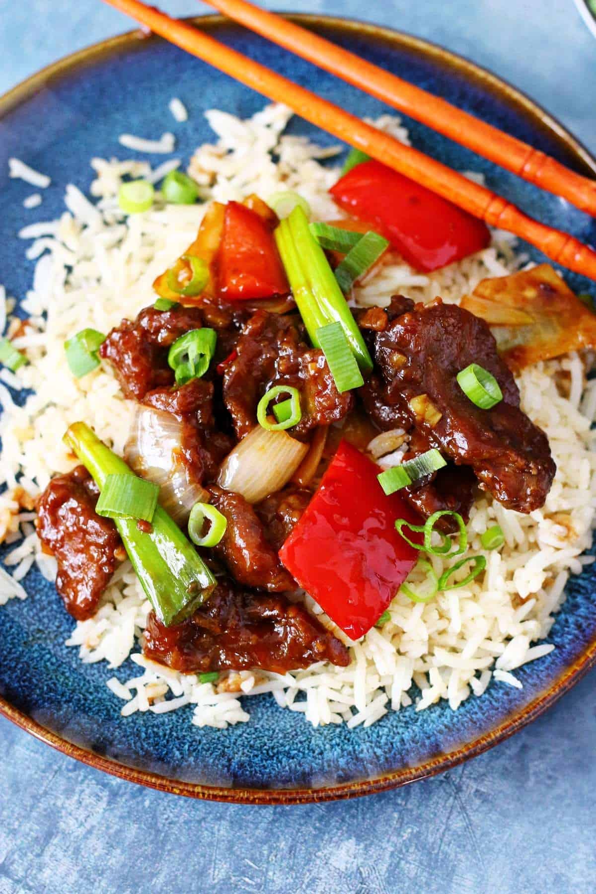 Crispy Beijing Beef with veggies on a bed of white rice and chopsticks on the side.