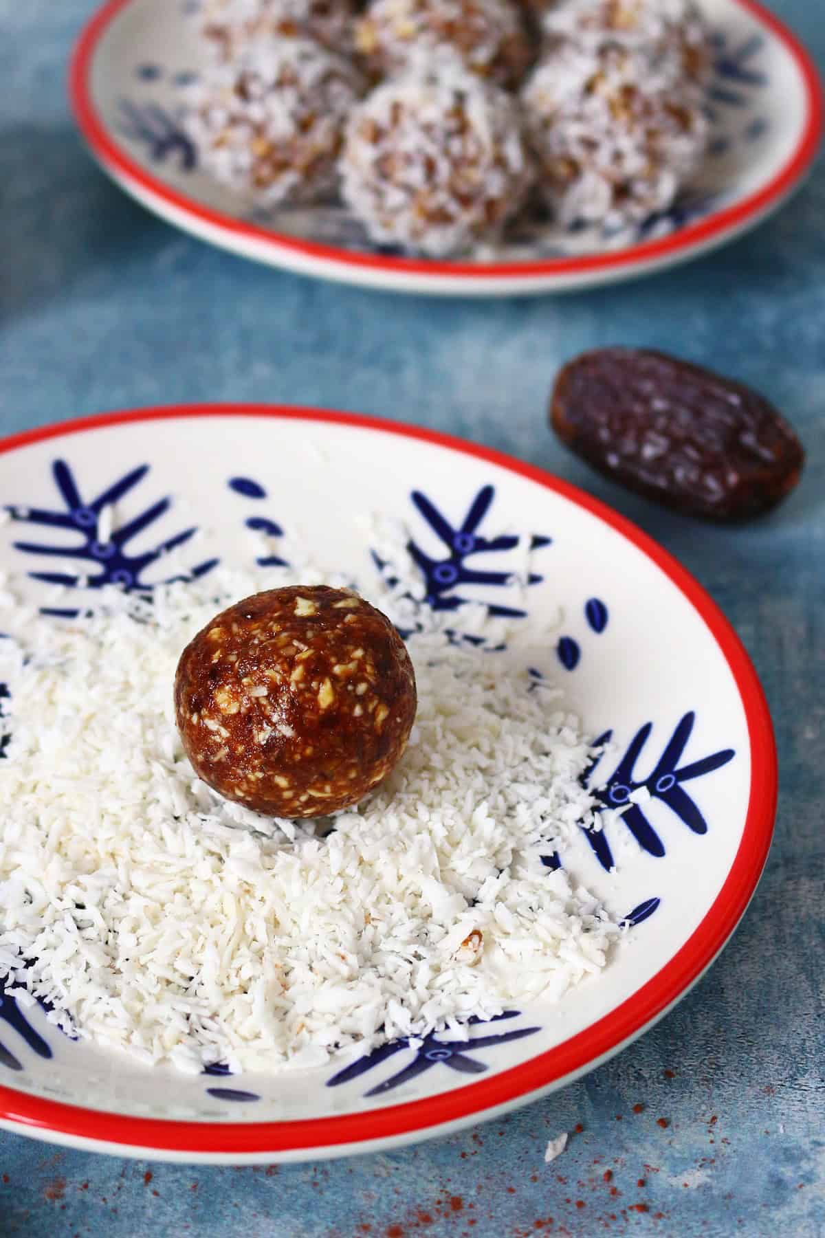 A date and nut ball on a plate with coconut flakes.