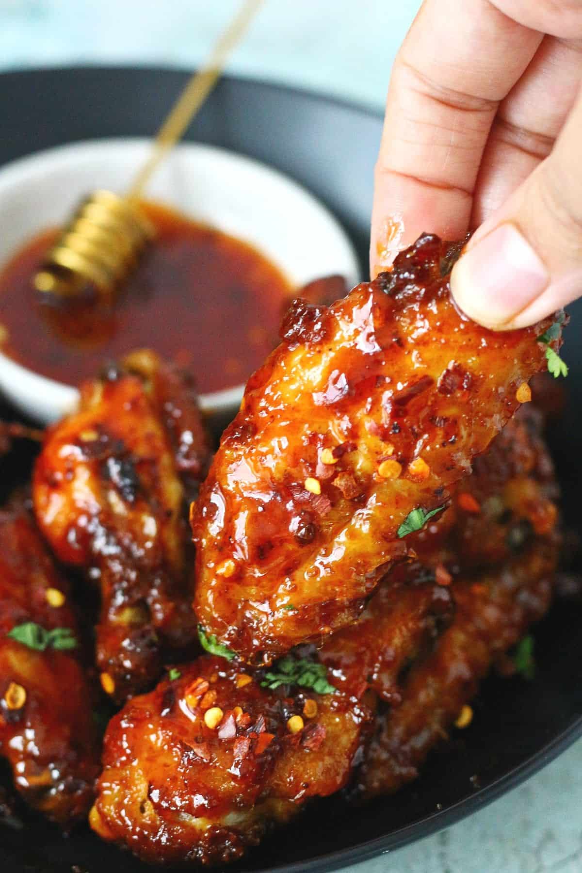 Holding a piece of sticky chicken wing with hot honey sauce at the back.