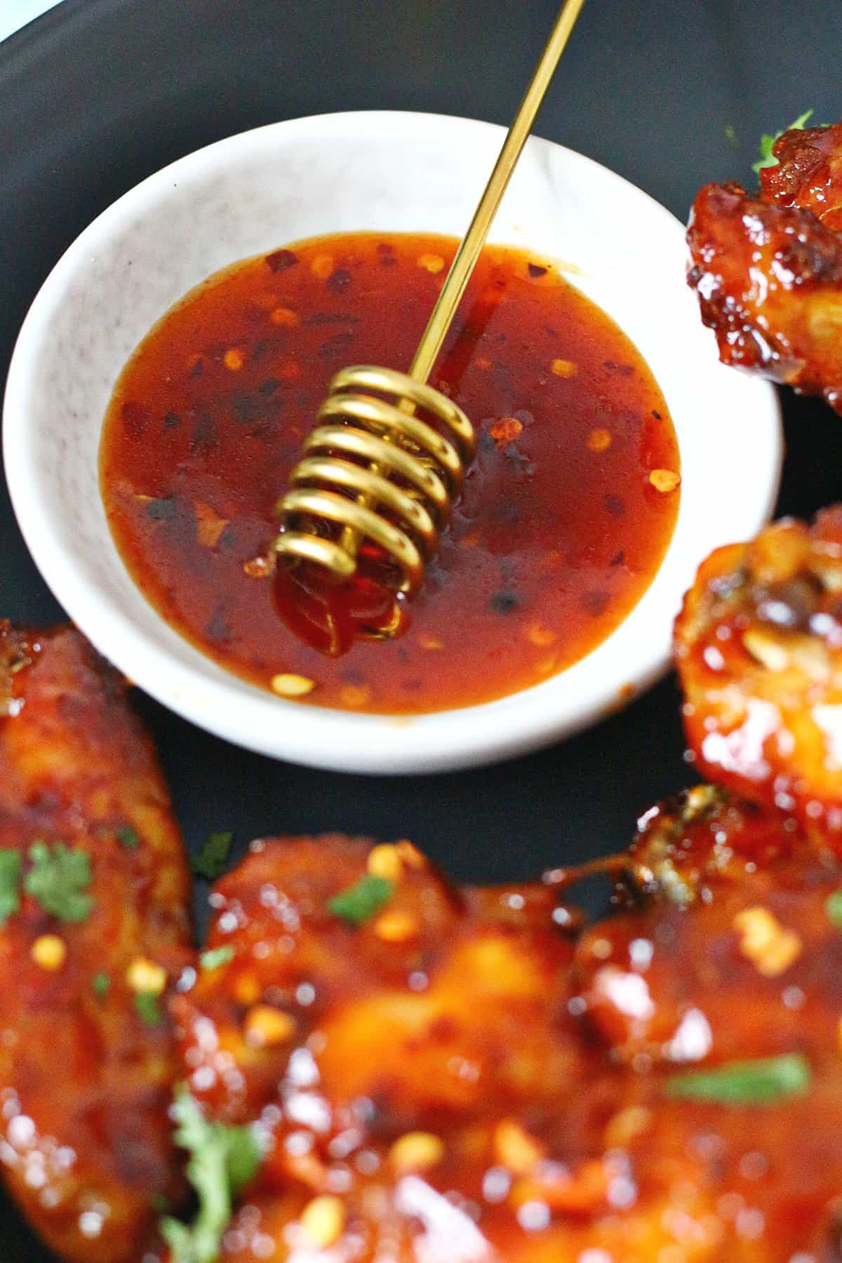 Hot honey sauce with dipper in a small bowl on top of a platter of sticky wings.