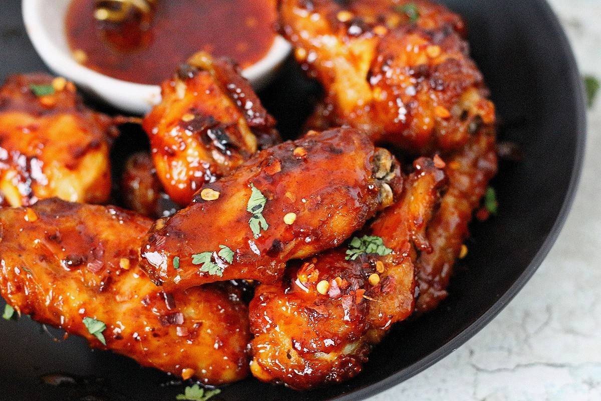 Sticky hot honey chicken wings in a shallow plated garnished with cilantro and spicy honey sauce at the back.