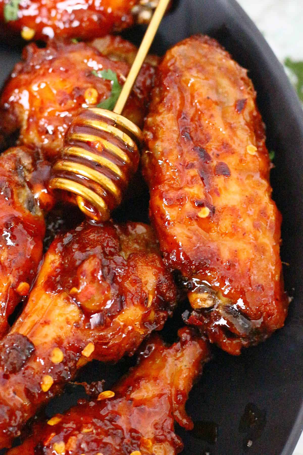 Close up of hot honey chicken wings with honey dipper between them.