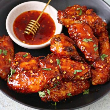 Hot honey chicken wings in a shallow plate with hot honey sauce on the side.