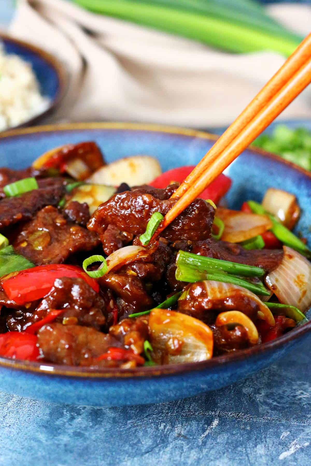 Picking up a piece of crispy beef with chopsticks from a plate of Beijing Beef.