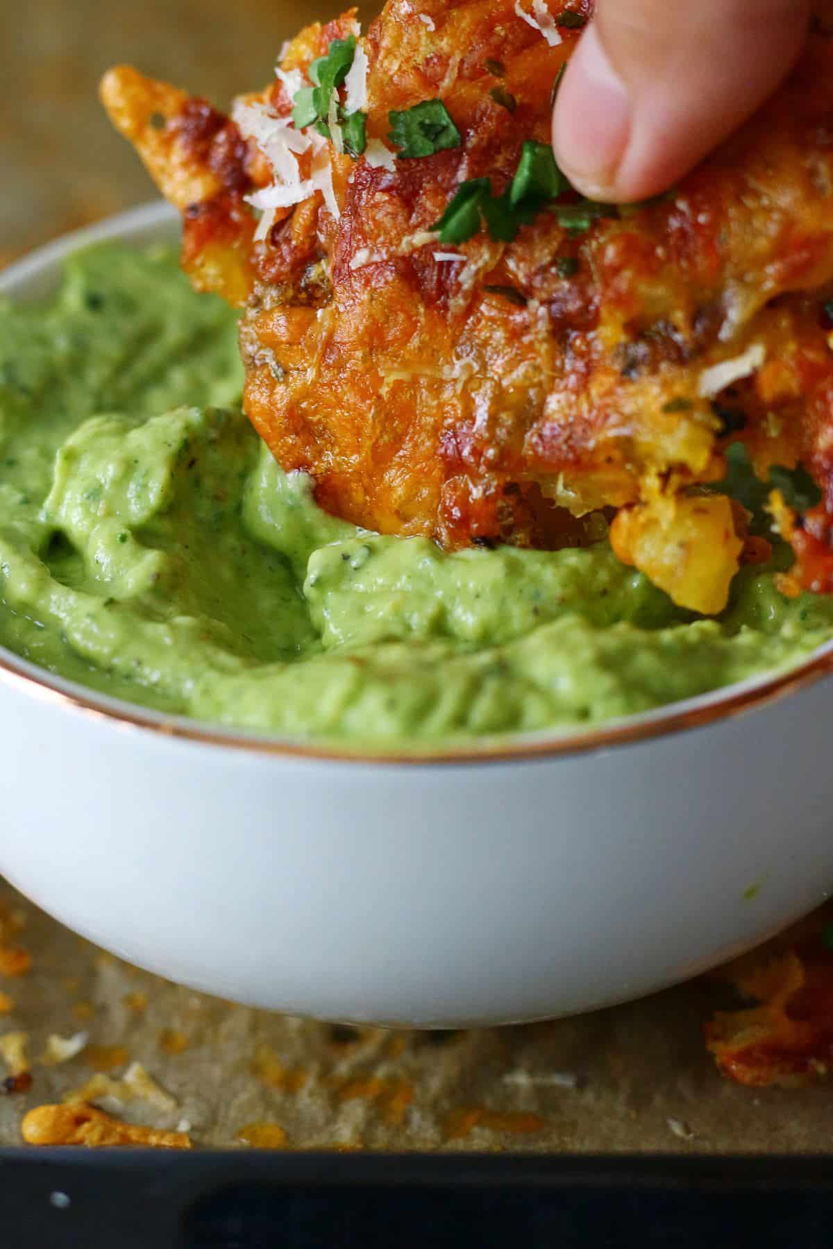 Dipping potato fritter in a bowl o avocado cream sauce.