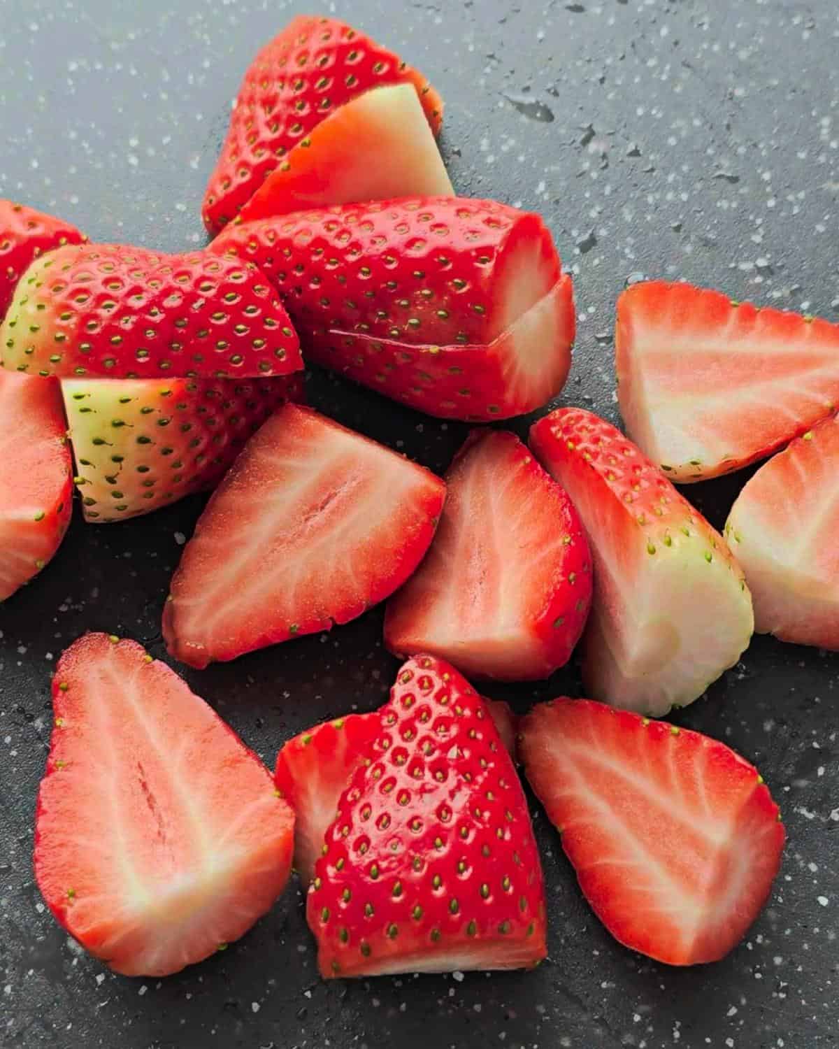 Sliced strawberries on a grey chopping board.