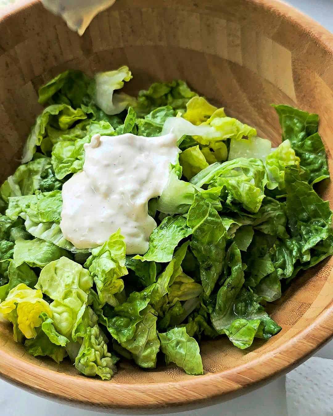 Chopped romaine lettuce in a salad bowl topped with caesar dressing.