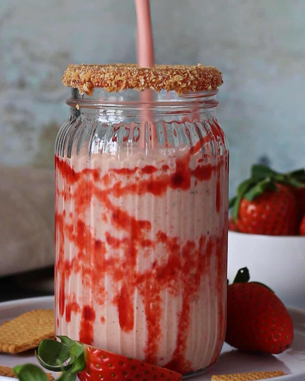 Pouring strawberry cheesecake milkshake in a decorated glass.