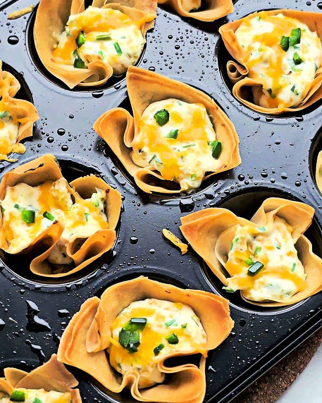 Baked jalapeno popper wonton cups in black muffin tray.