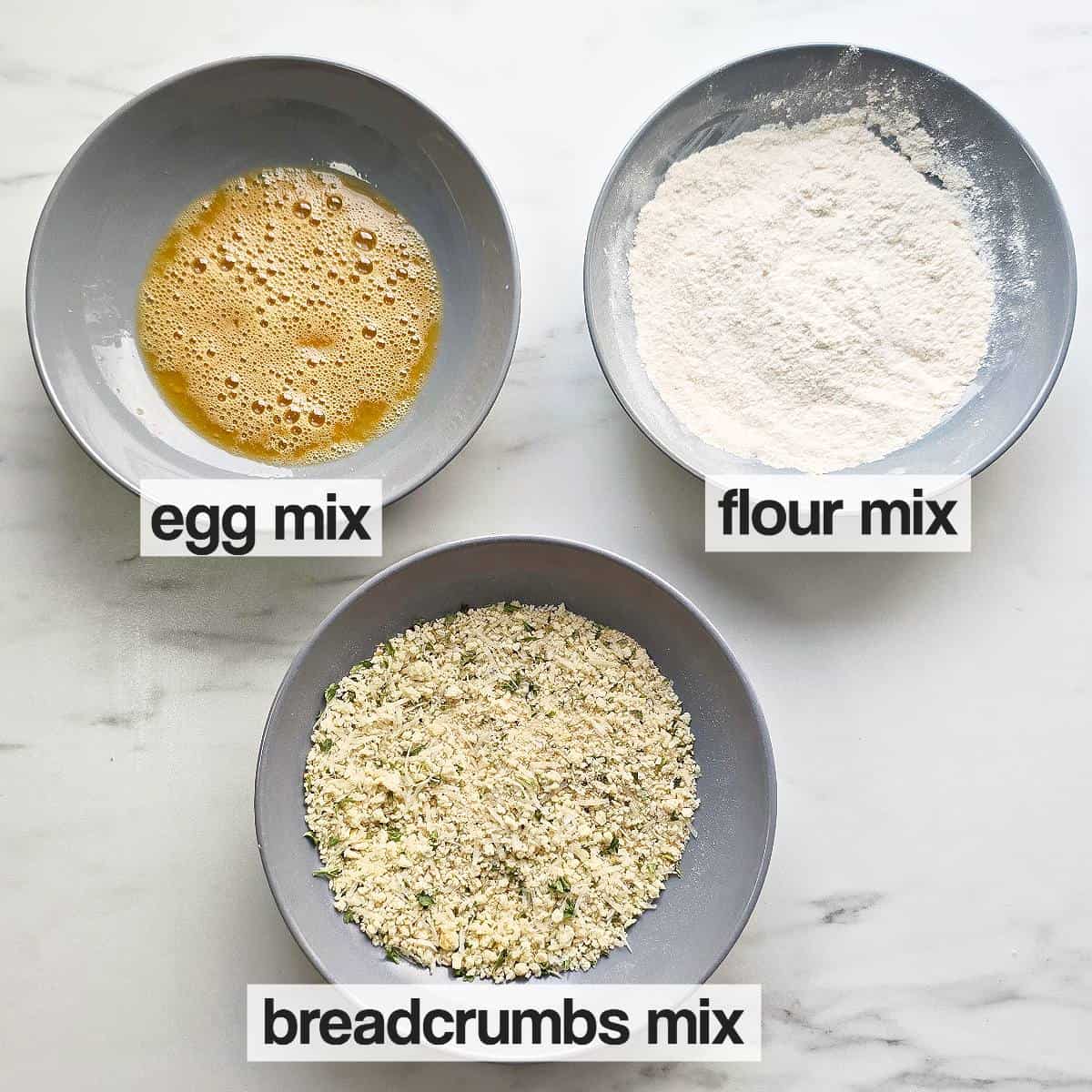 Breading station with three bowls of seasoned breadcrumbs, flour and eggs.