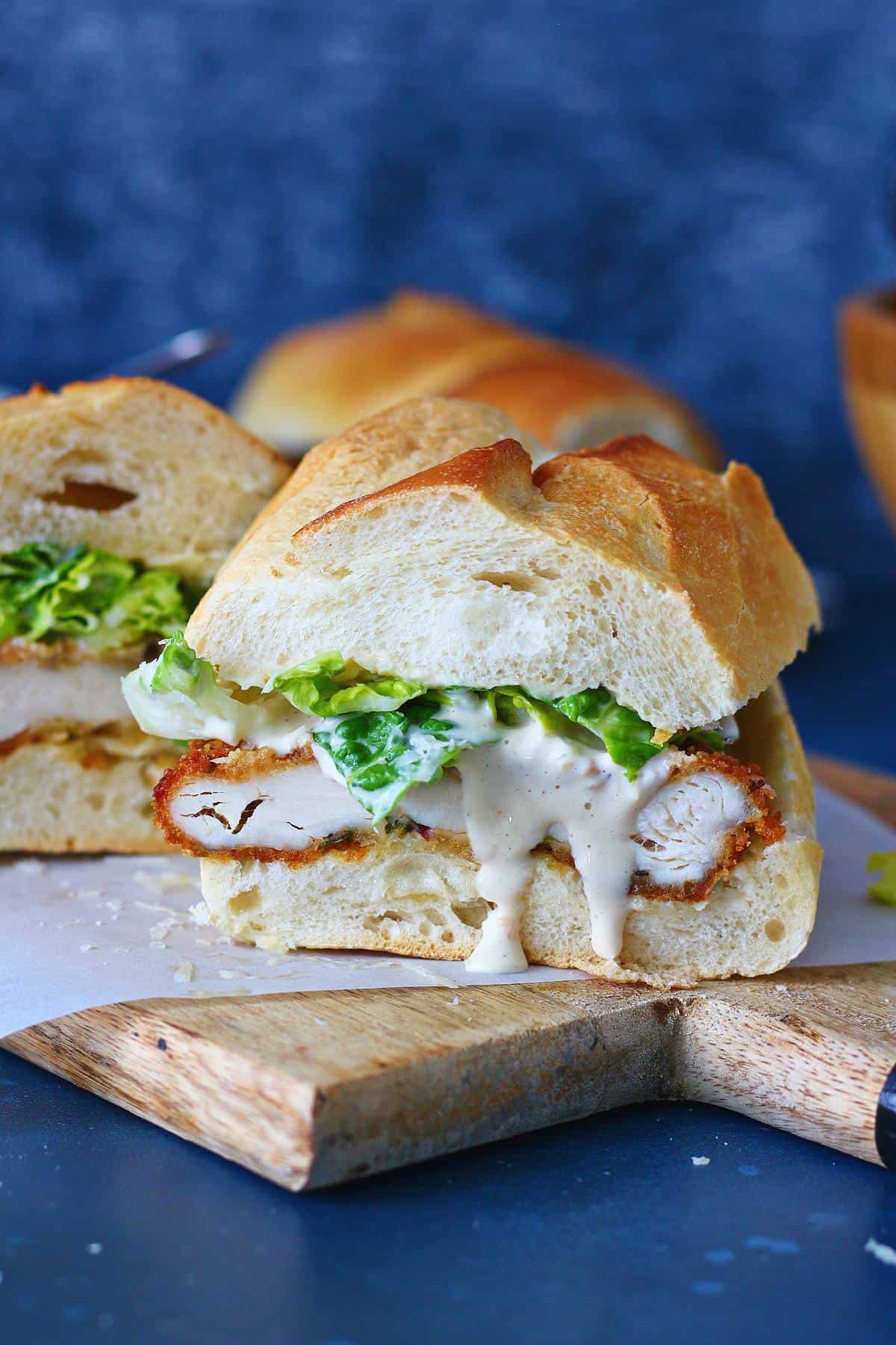 A sliced crispy chicken sandwich with its dressing oozing.