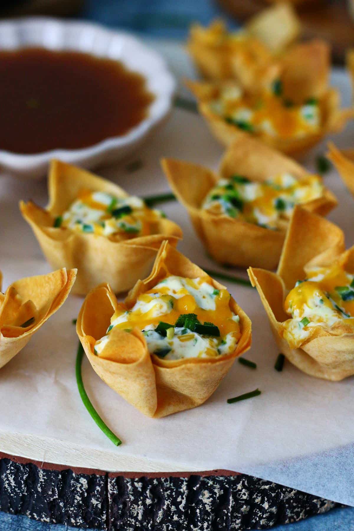 Jalapeno popper wonton cups from the side on a wooden serving board.