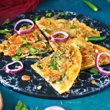 Quarters of egg paratha on a black dish garnished with red onion rings.