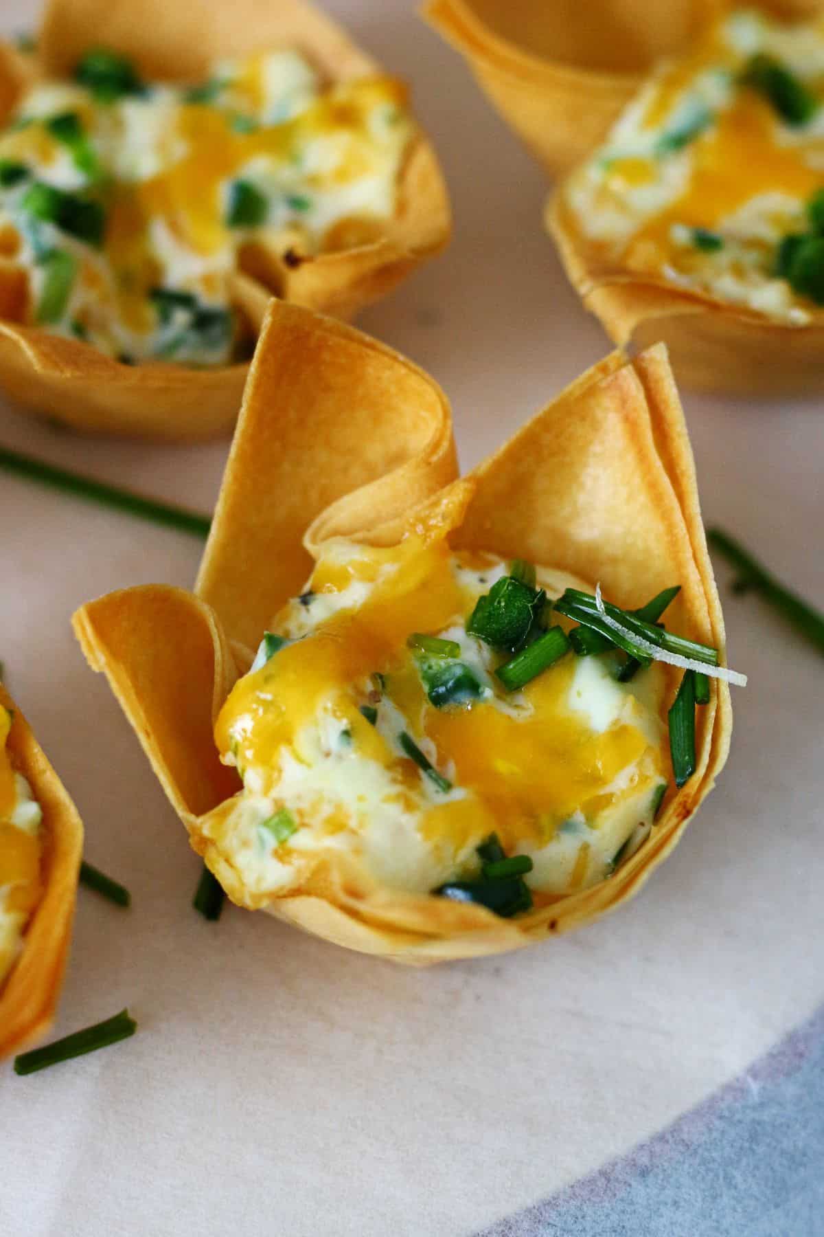 Close up of wonton cup with cream cheese filling, melted cheddar and diced jalapeno.