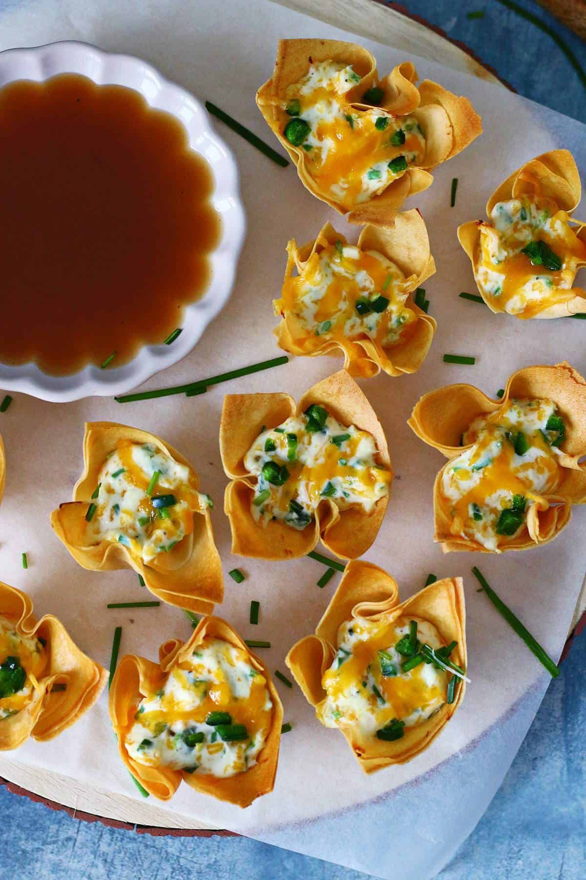 Overhead sot of jalapeno wontons garnished with chives with a sauce on the side.