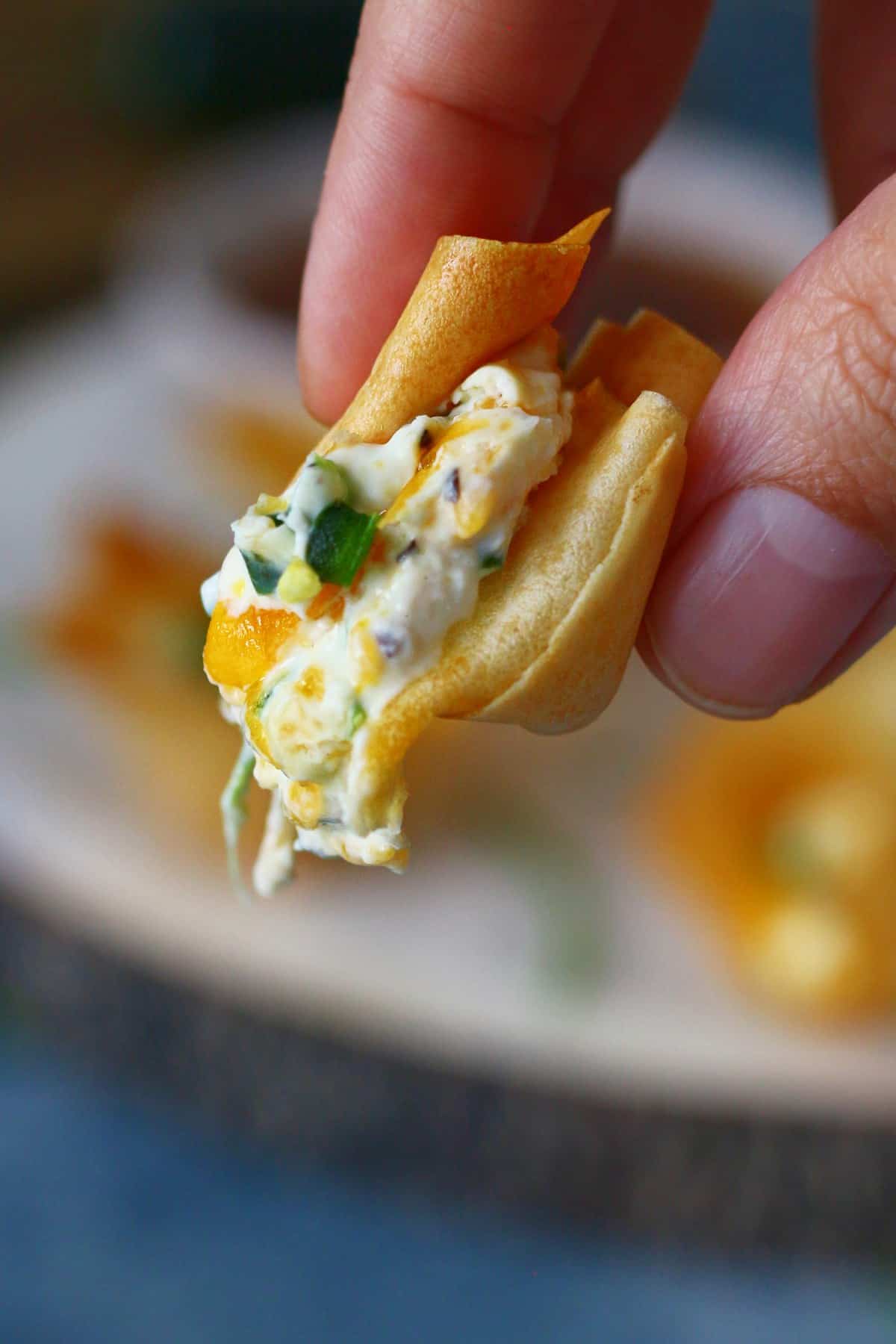 Holding a broken cream cheese wonton with oozing filling.