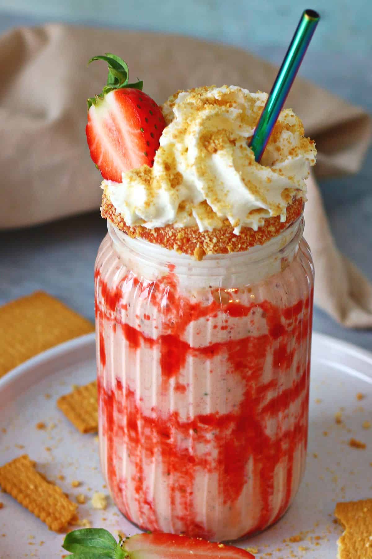 Strawberry cheesecake milkshake in a tall glass with whipped cream, fresh strawberry and a straw.