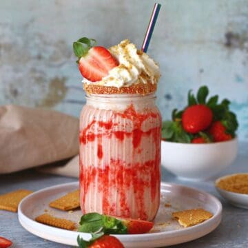 Strawberry cheesecake milkshake in a tall glass with whipped cream and a straw.