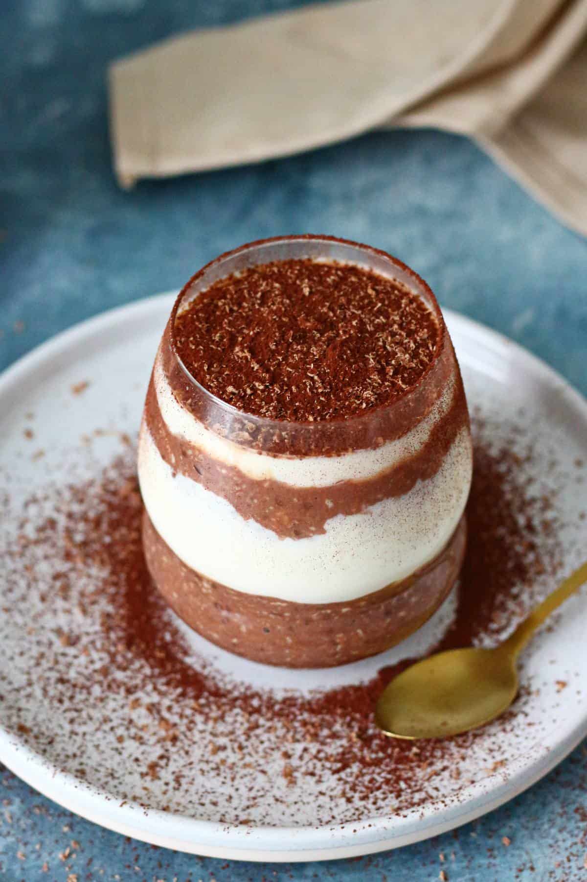 Layers of tiramisu overnight oats in glass with a gold spoon on the side.