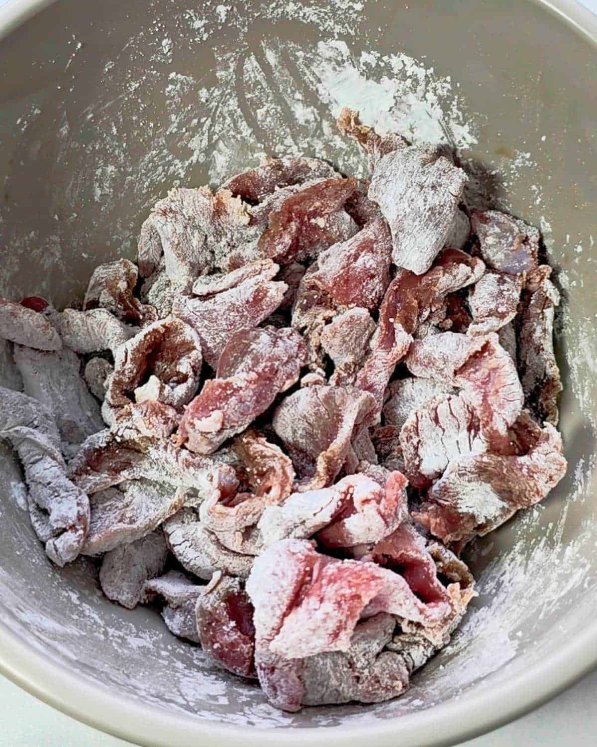 Marinated beef strips in a grey bowl.