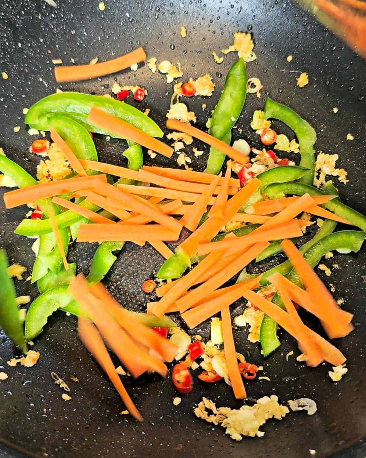 Sliced carrot, bell pepper and aromatics in a wok.