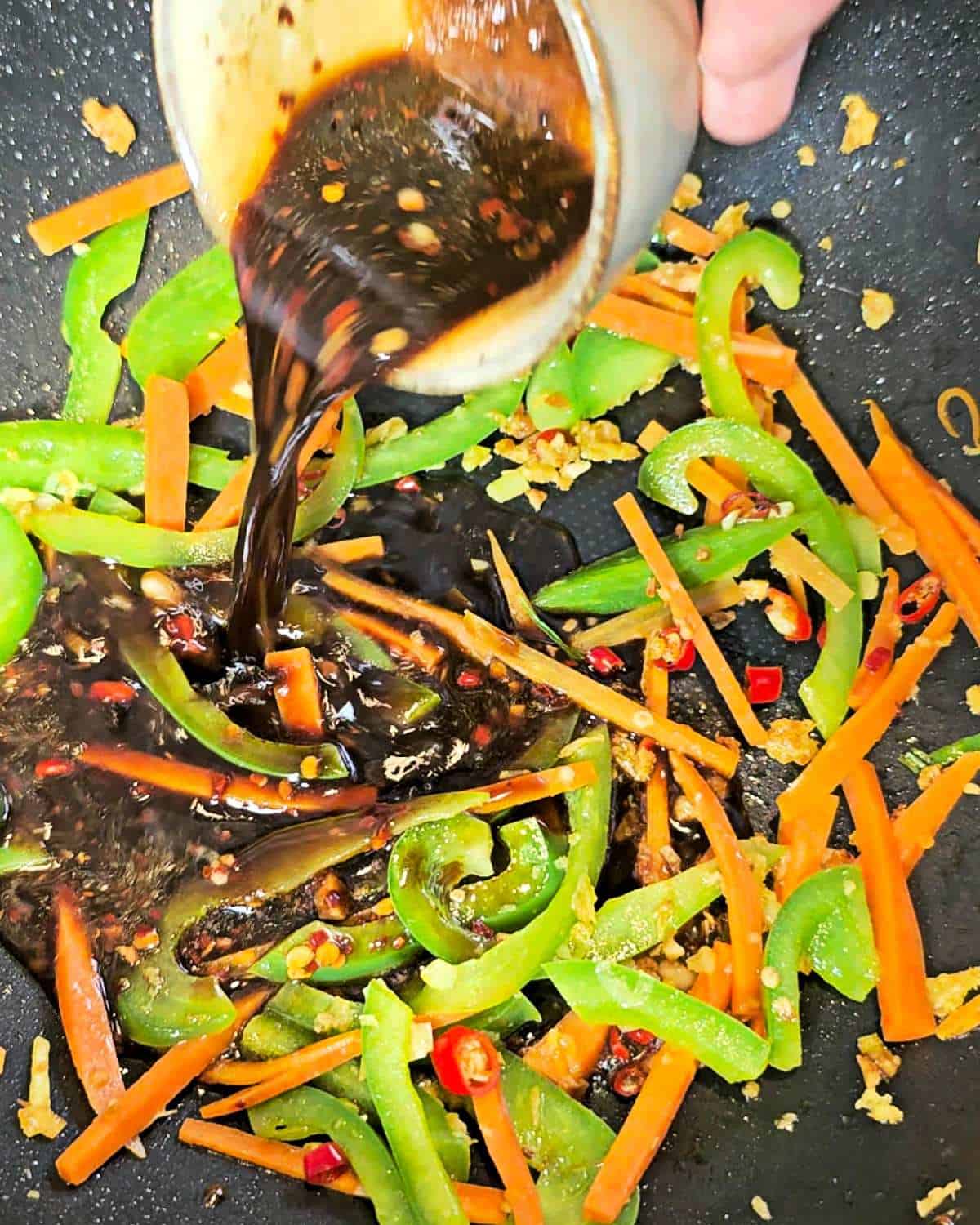 Pouring Mongolian beef sauce over the veggies in a wok.