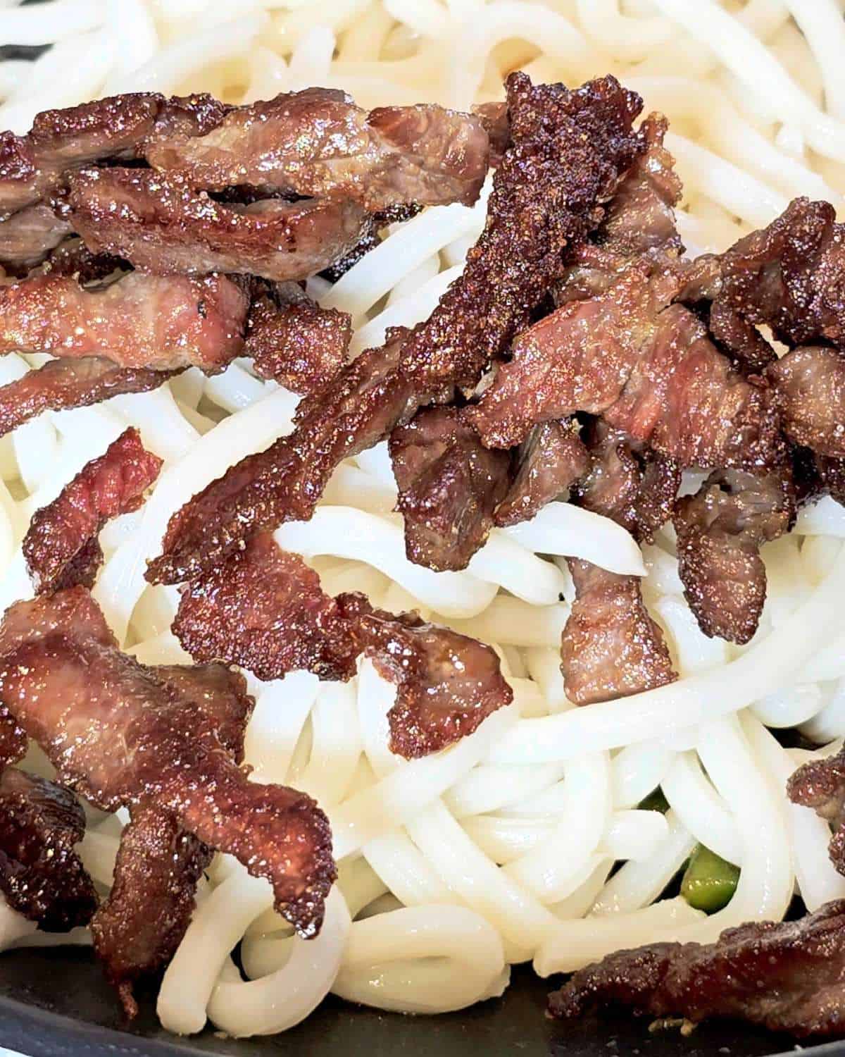 Cripsy fried beef and udon noodles in a wok.