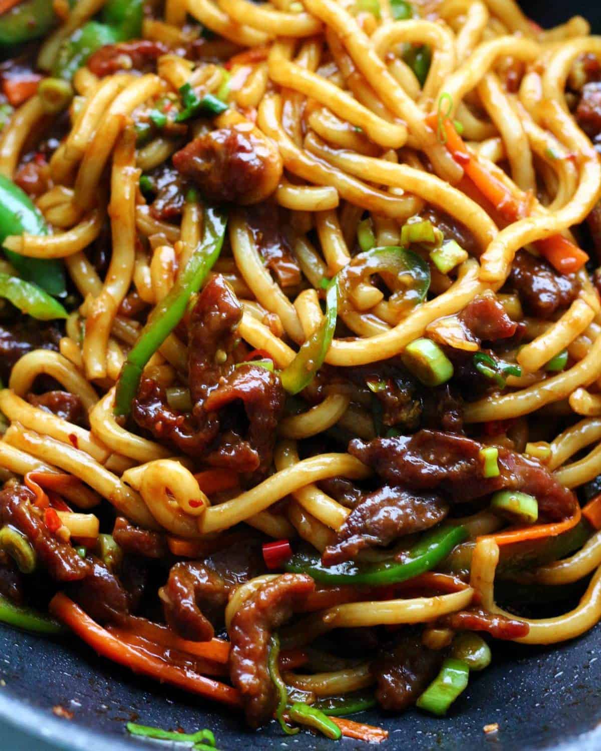 Udon noodles tossed with beef and veggies in a wok.