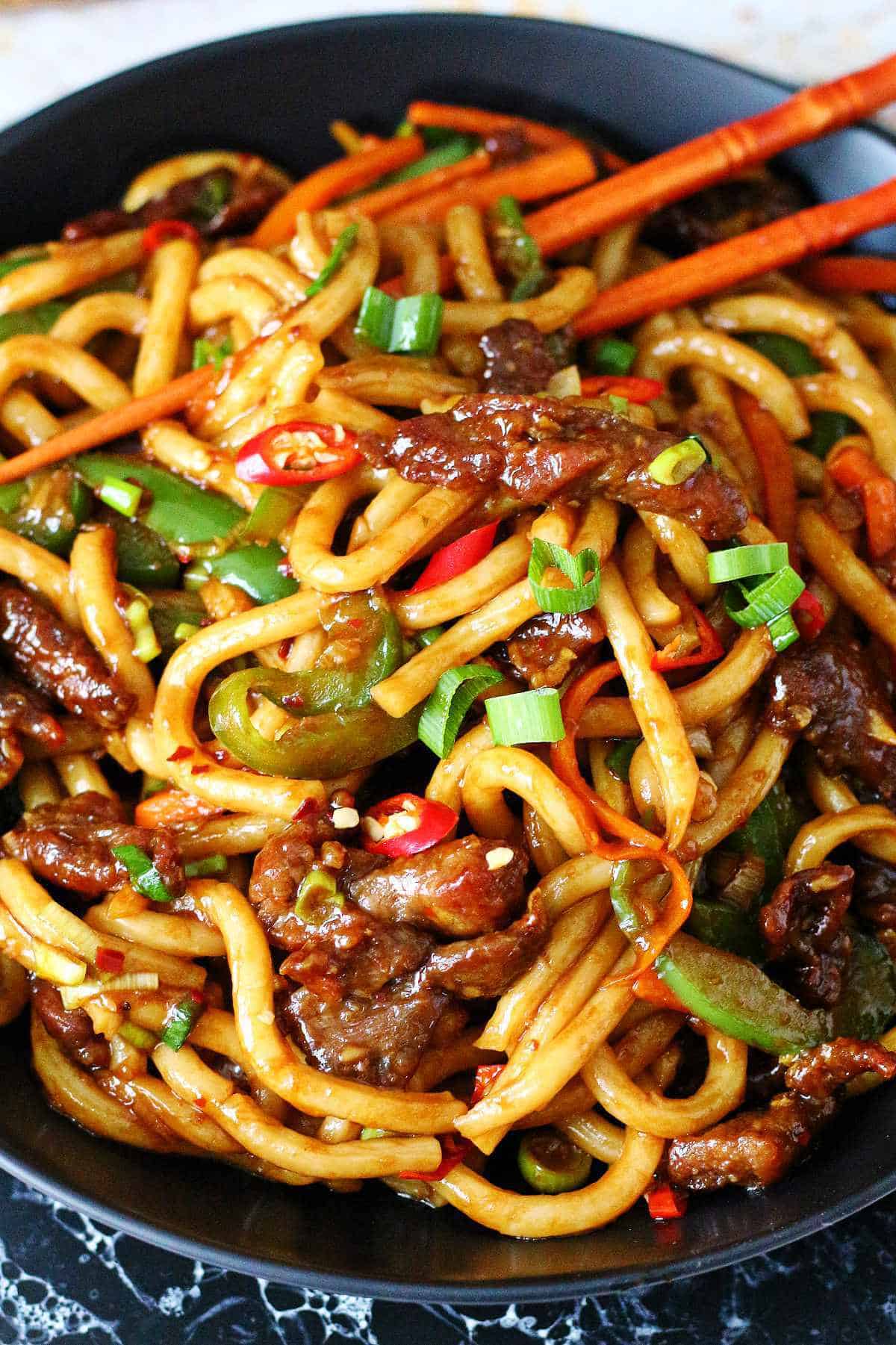 Close up of mongolian noodles with beef and veggies in a black dish.