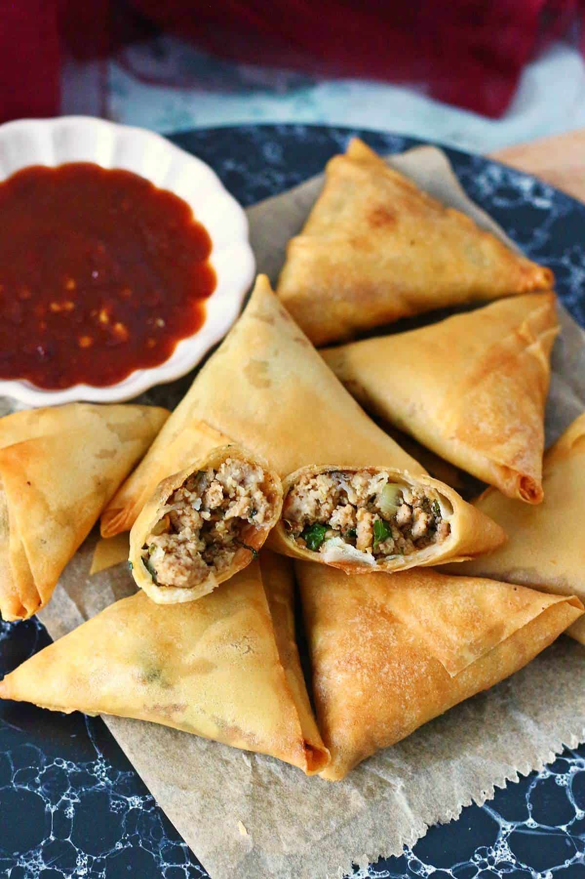 Broken apart samosa with inside keema filling shown, surrounded by other fried samosas.