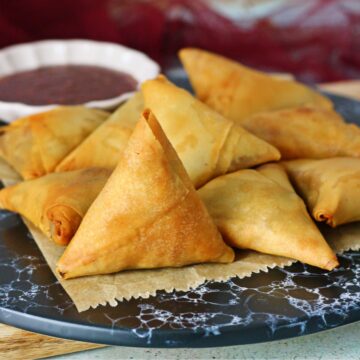 A dish of keema samosas with a small bowl of dipping sauce at the back.