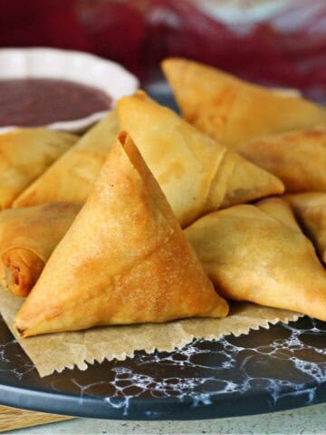 A dish of keema samosas with a small bowl of dipping sauce at the back.