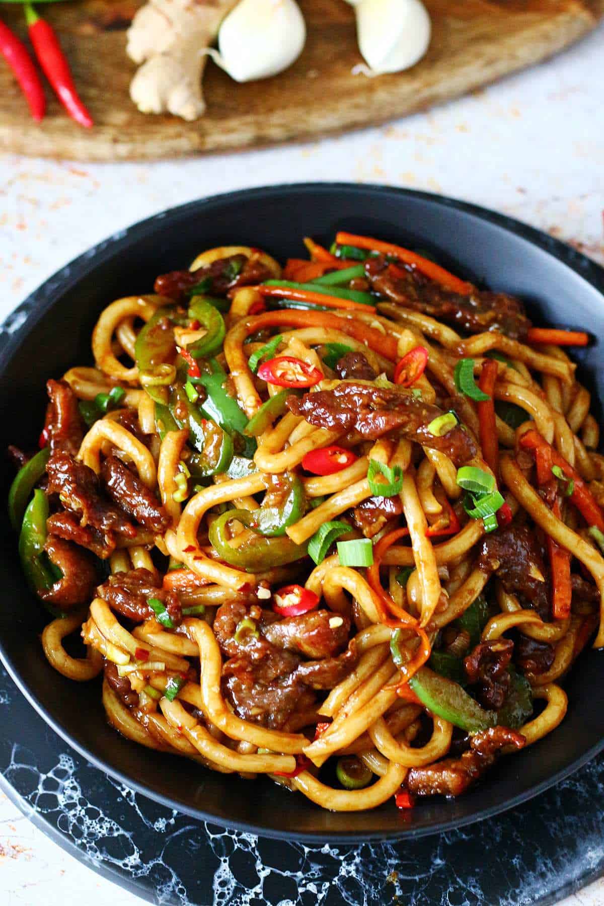 Glossy Mongolian beef noodles with vegetables in a black dish.