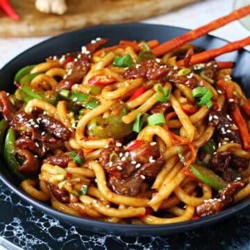 A black dish of Mongolian beef noodles with chopsticks inside.