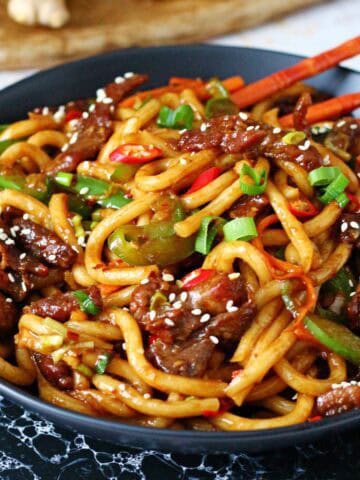 A black dish of Mongolian beef noodles with chopsticks inside.