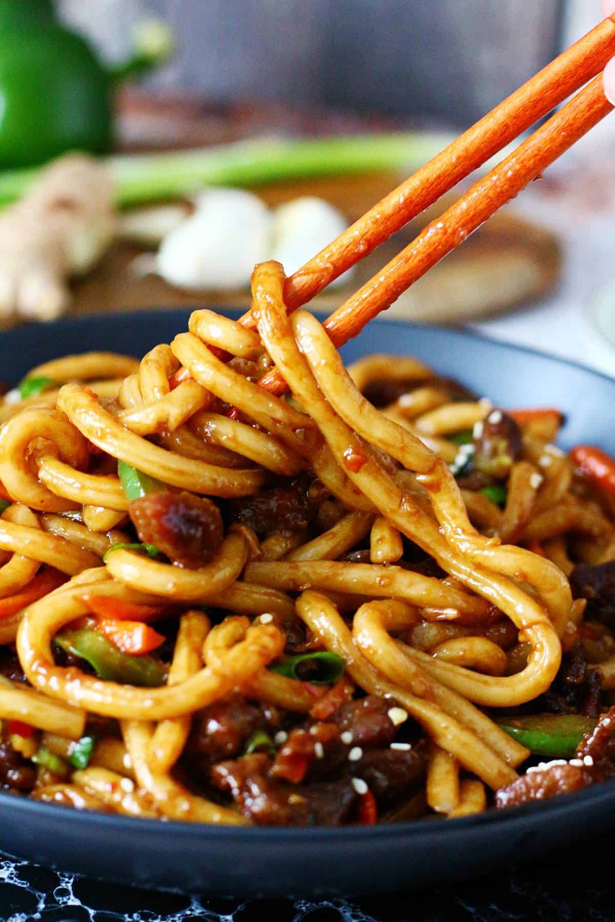 Swirling beef udon noodles in chopsticks.